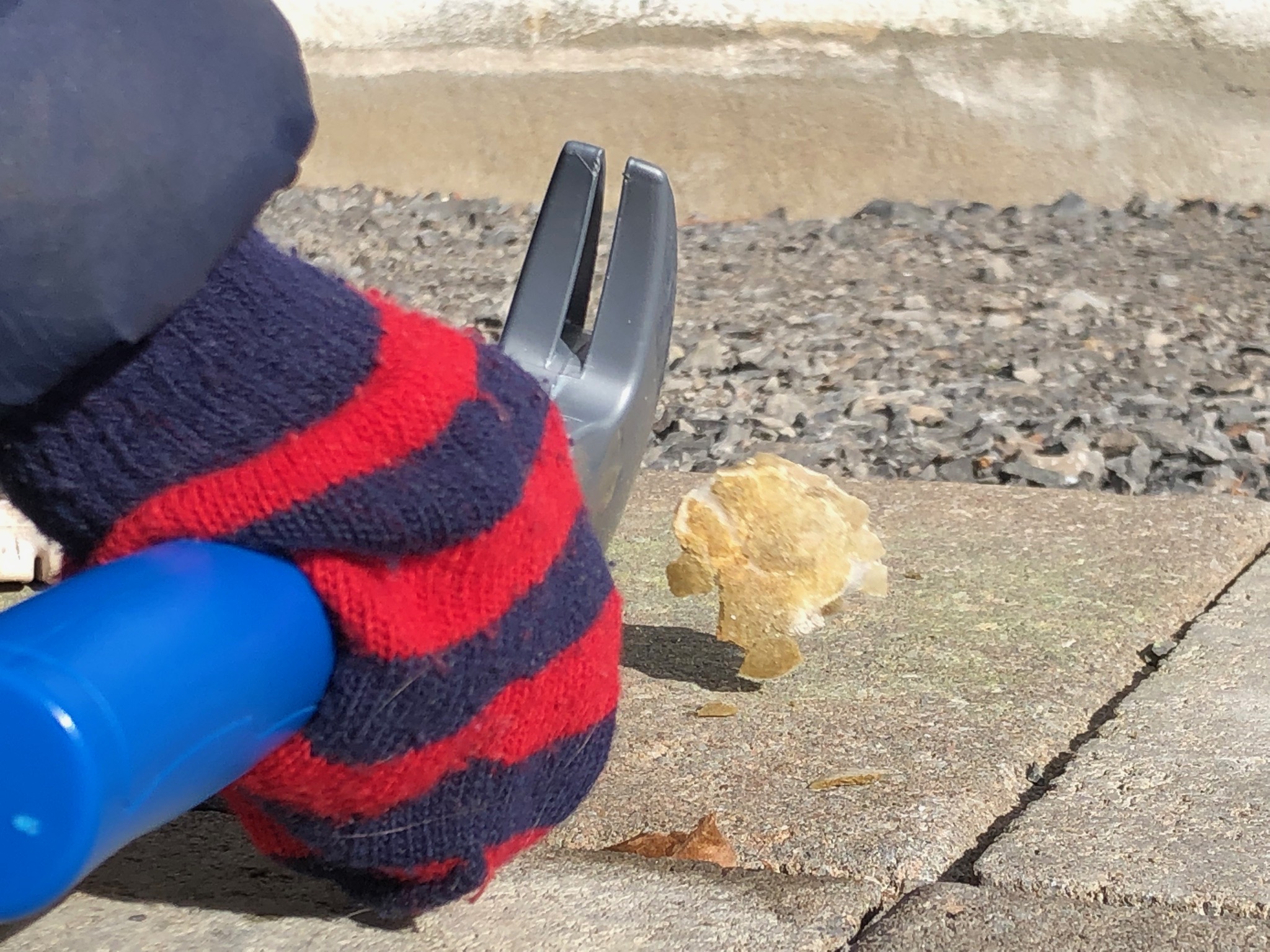 A child's hand wearing a striped red and navy gloves holds a blue and grey plastic hammer. A fabricated moon rock is seen next to it, in motion, after being smashed