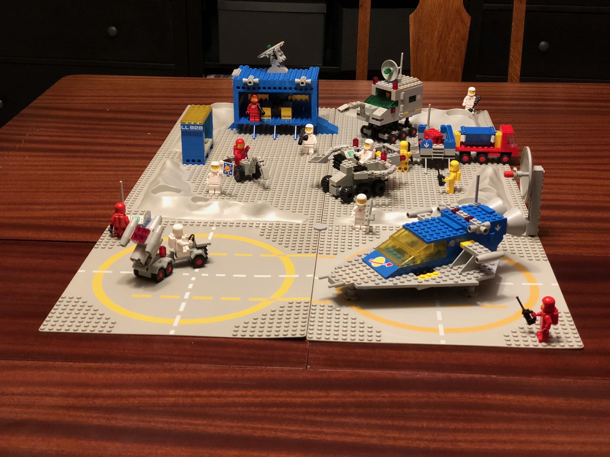 A collection of vintage space lego sets sitting on four grey lego boards, atop a dining table