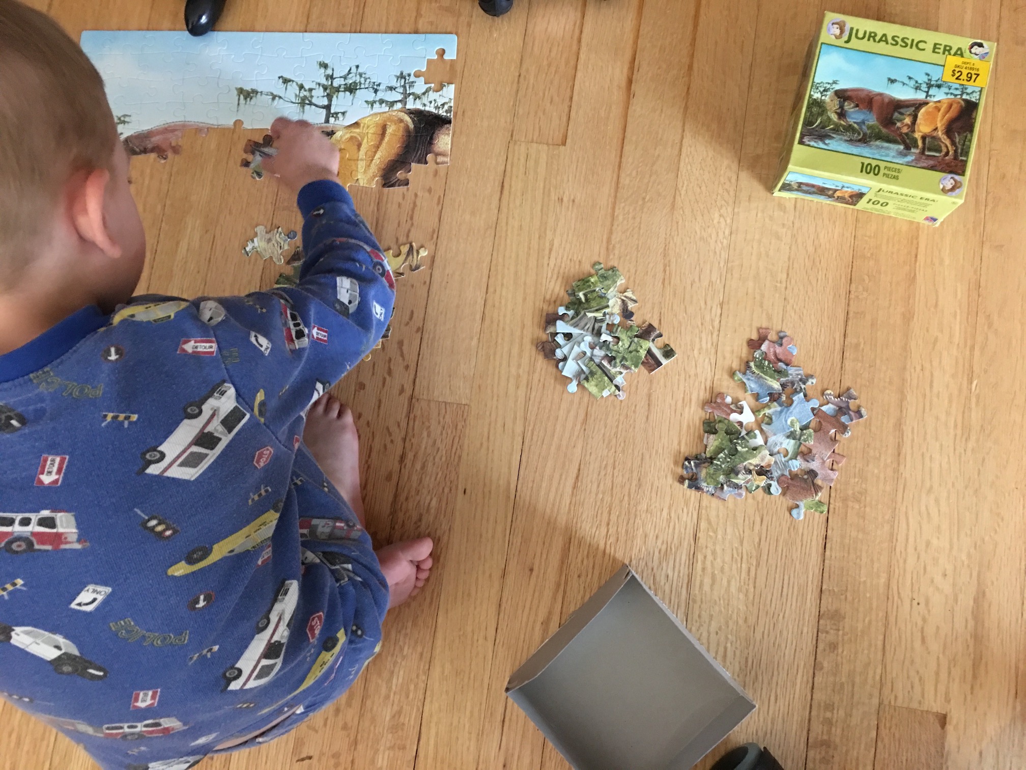 A young boy is putting together a puzzle from the jurassic era. Piles of sorted puzzle pieces sit beside him.