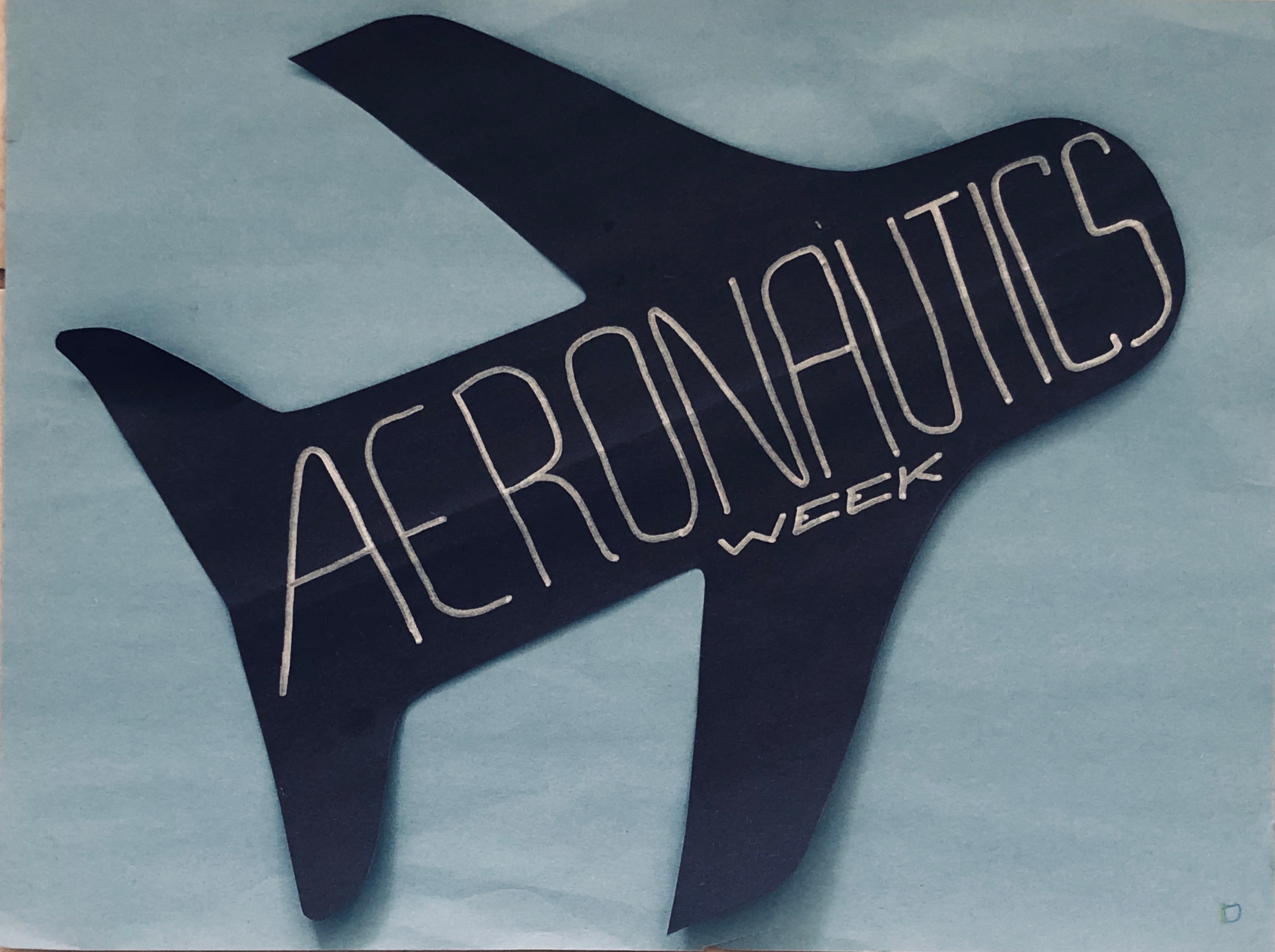 Image of an airplane cut out of black construction paper with the words Aeronautics Week written in silver sharpie